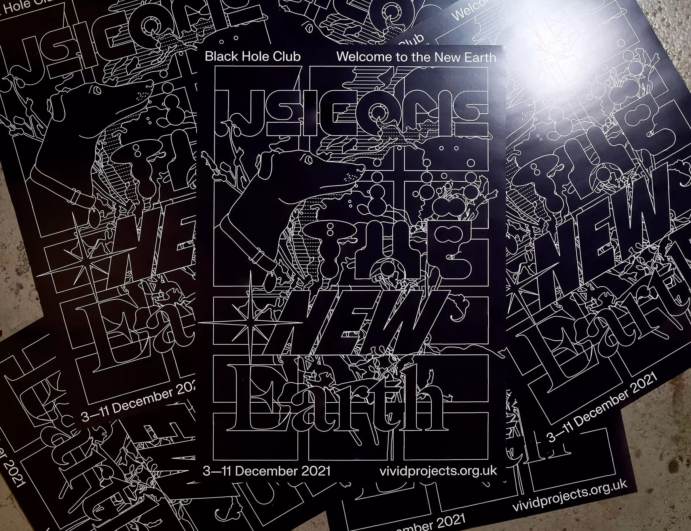 Scattered, glossy black posters. with a dense line illustration, and the title 'Welcome to the New Earth'.